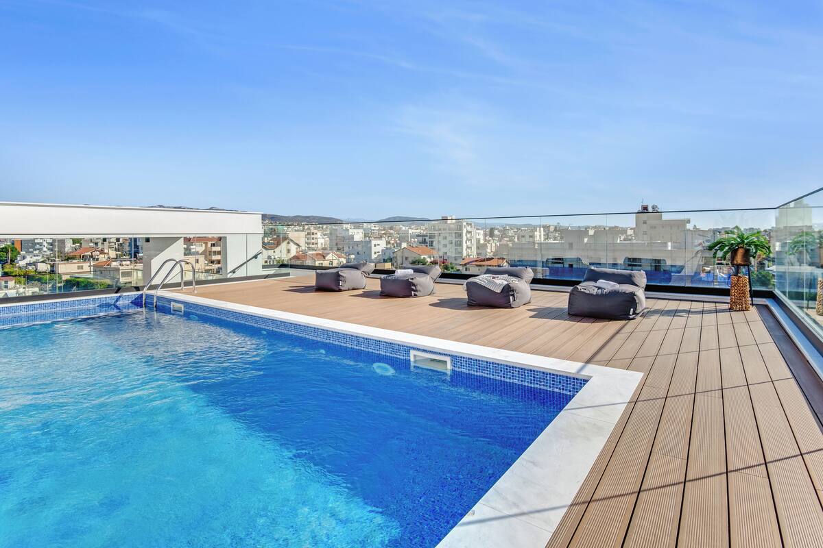 A rooftop swimming pool with lounge chairs and a city view.