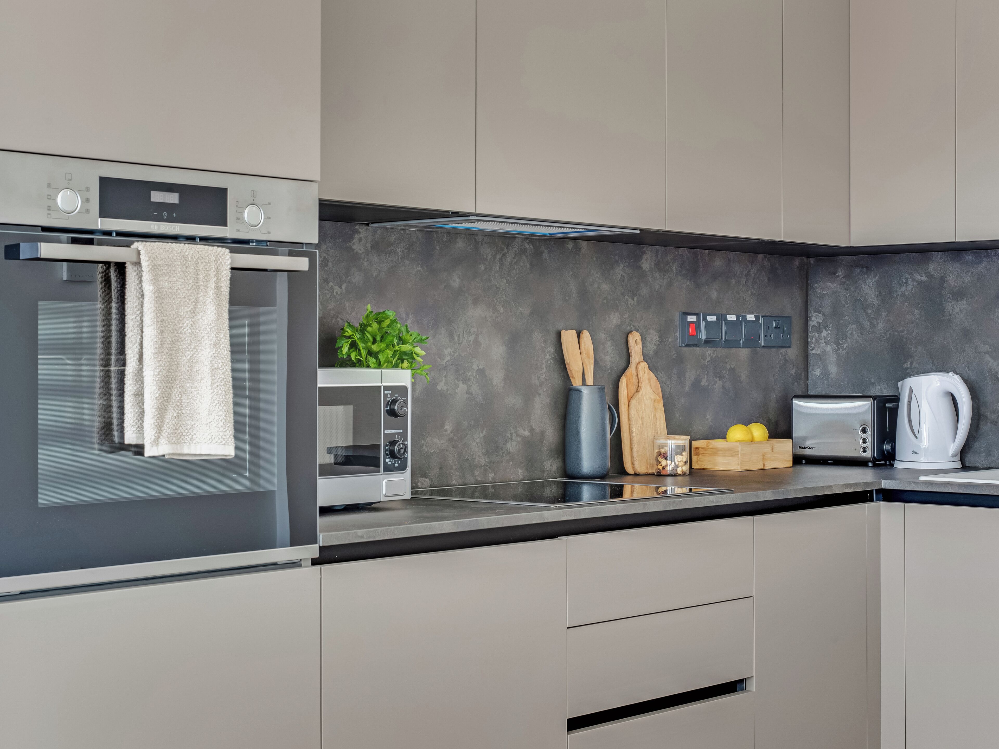 A modern kitchen with a built-in oven, microwave, and toaster. There are wooden utensils, a coffee maker, and a plant on the counter.