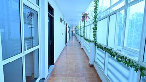 A long, narrow hallway with tiled flooring, large windows on both sides, and hanging plants. - Date Palm Hotel (Gurugram)