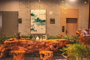 A wooden dining table with a rustic design, surrounded by plants and a painting on the wall. - Jibolong Hotel (Lijiang)