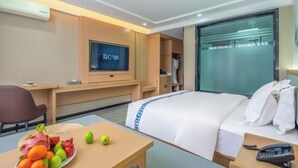 A hotel room with a bed, a desk, a television, and a fruit bowl. - Jibolong Hotel (Lijiang)