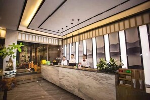 A reception area with a marble counter, a plant, and a view of the interior through large windows. - Jibolong Hotel (Lijiang)