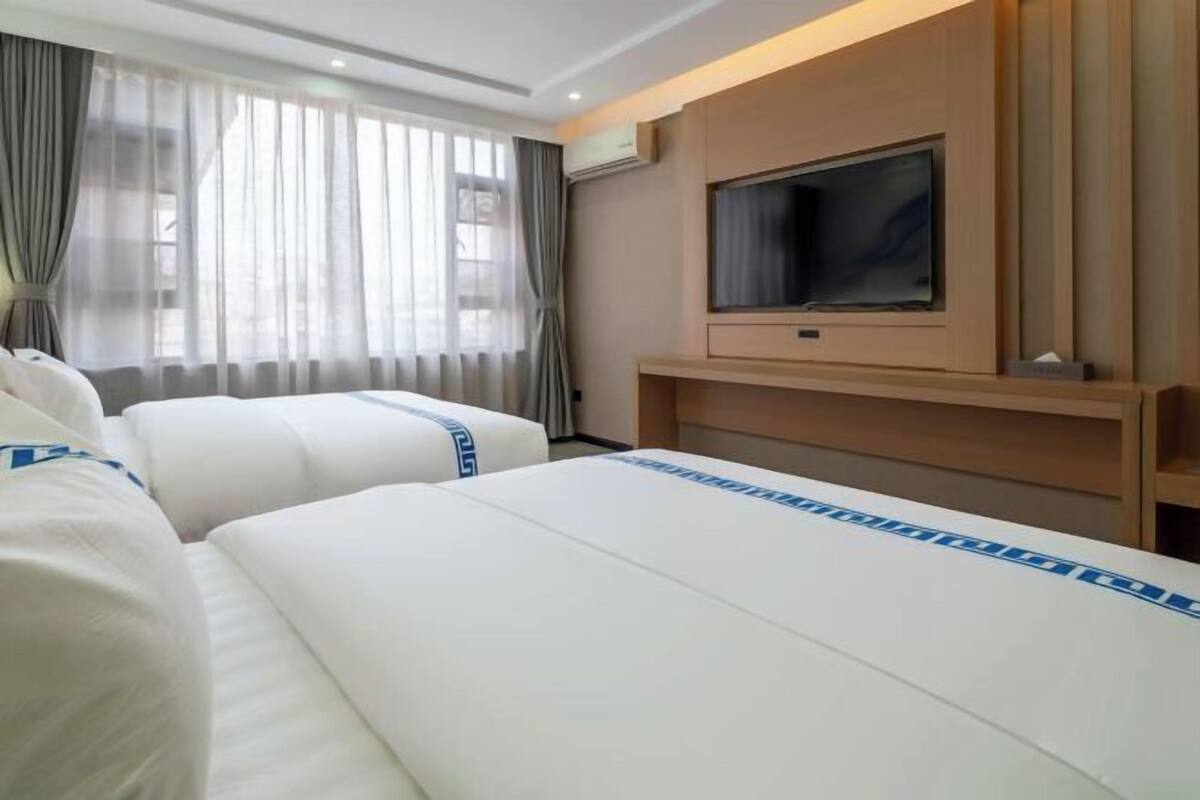 A hotel room with two beds, a TV, and a window with curtains.