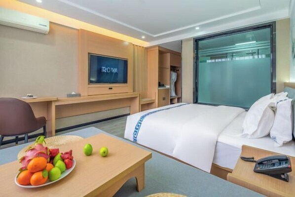 A hotel room with a bed, a desk, a television, and a fruit bowl. - Jibolong Hotel (Lijiang)