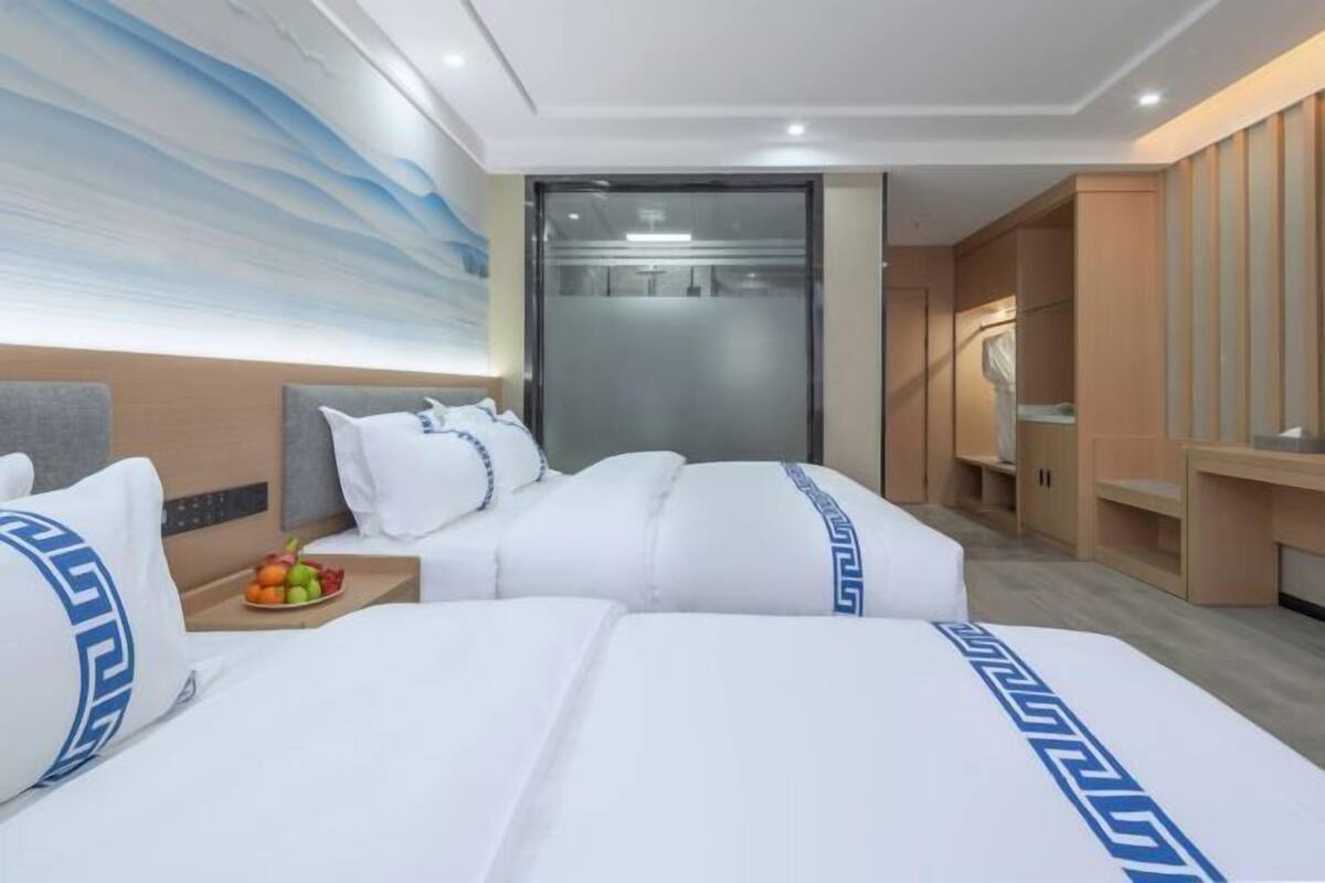 A hotel room with two beds, a large wall mural, a sliding door, and a small table with fruit.