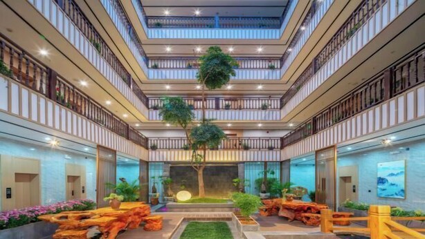 A modern hotel atrium with multiple floors, a central garden, and a variety of plants and decorative elements. - Jibolong Hotel (Lijiang)