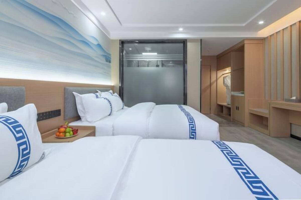 A hotel room with two beds, a large wall mural, a sliding door closet, and a small table with fruit.
