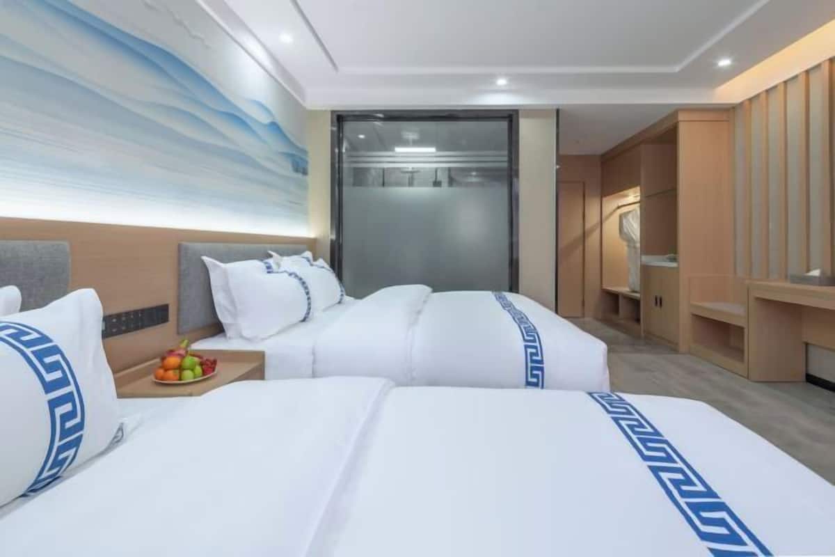 A hotel room with two beds, a large wall mural, a sliding door closet, and a small table with fruit.