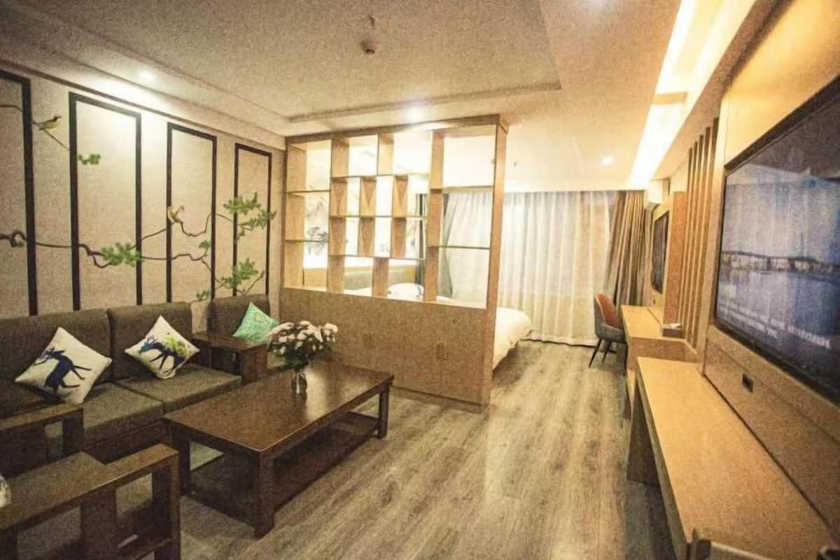A modern hotel room with a sofa set, a coffee table, a TV, and a large window with curtains.