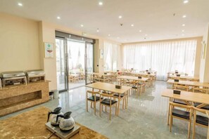 A hotel dining area with multiple tables and chairs, a buffet station, and a large window with curtains. - Jibolong Hotel (Lijiang)