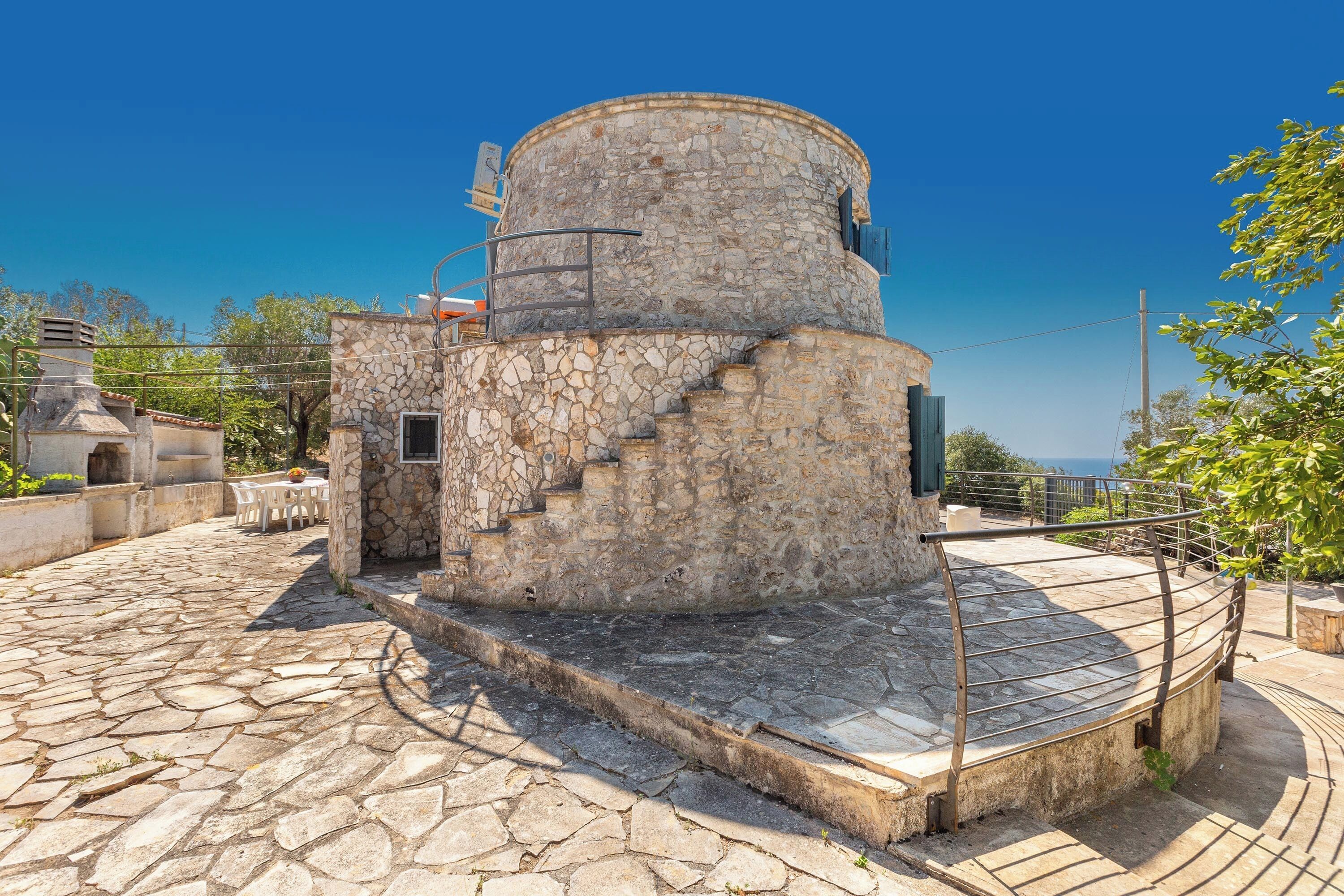 Una torre de piedra con una escalera en espiral, un patio de piedra y vistas al mar.