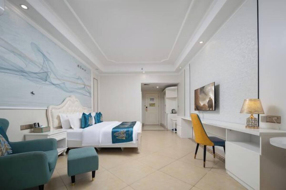 Une chambre d’hôtel avec un lit, un bureau, une chaise, une télévision et un grand tableau abstrait accroché au mur.