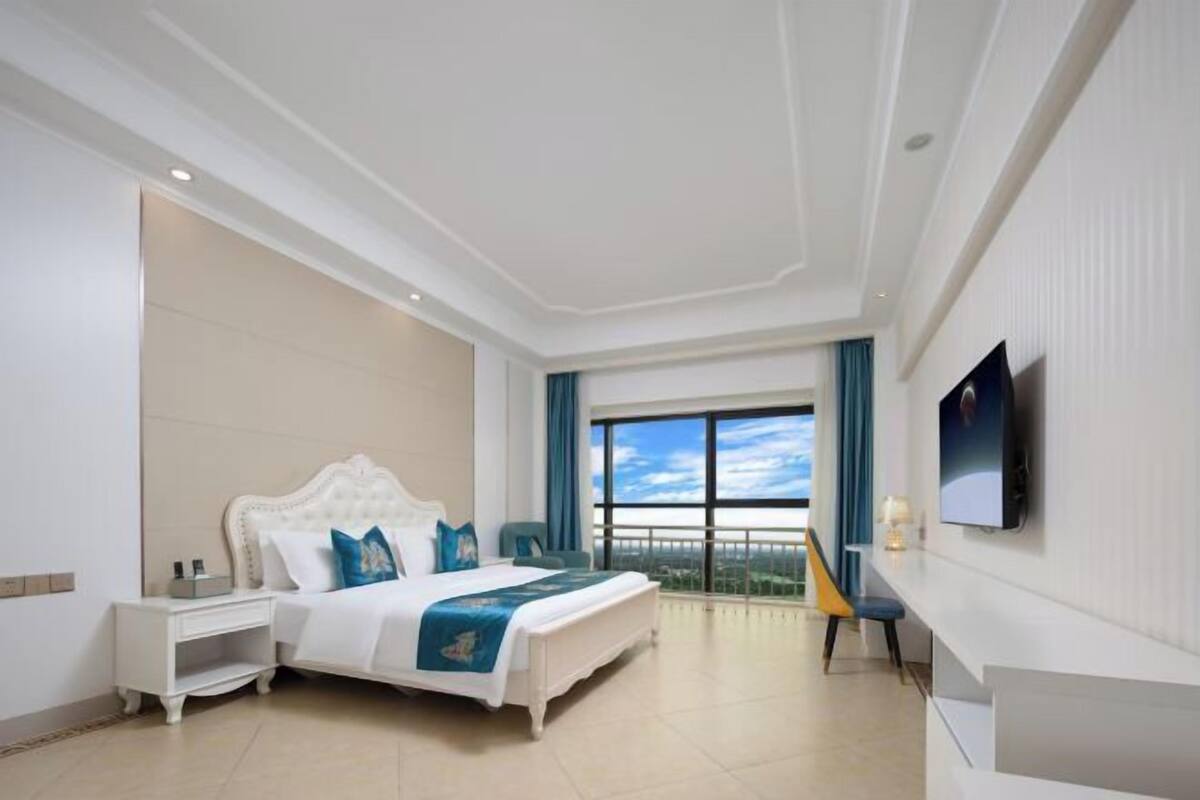 Une chambre d’hôtel avec un grand lit, une table de chevet, un téléviseur fixé au mur et une fenêtre donnant sur un beau paysage.