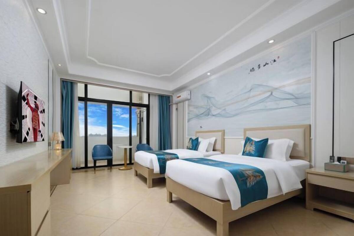 Une chambre d’hôtel avec deux lits, un bureau, une chaise et une grande fenêtre donnant sur un beau paysage.