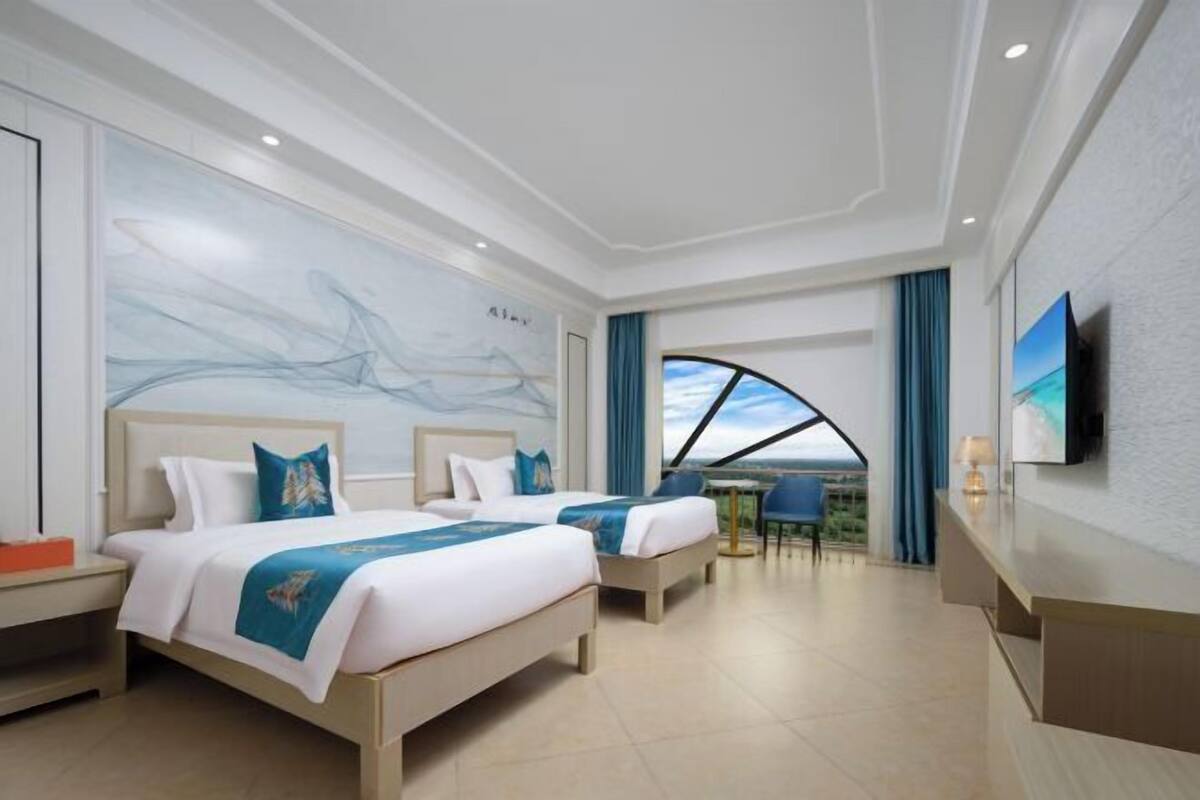 Une chambre d’hôtel avec deux lits, une grande fresque murale abstraite, une vue sur le ciel et un téléviseur fixé au mur.