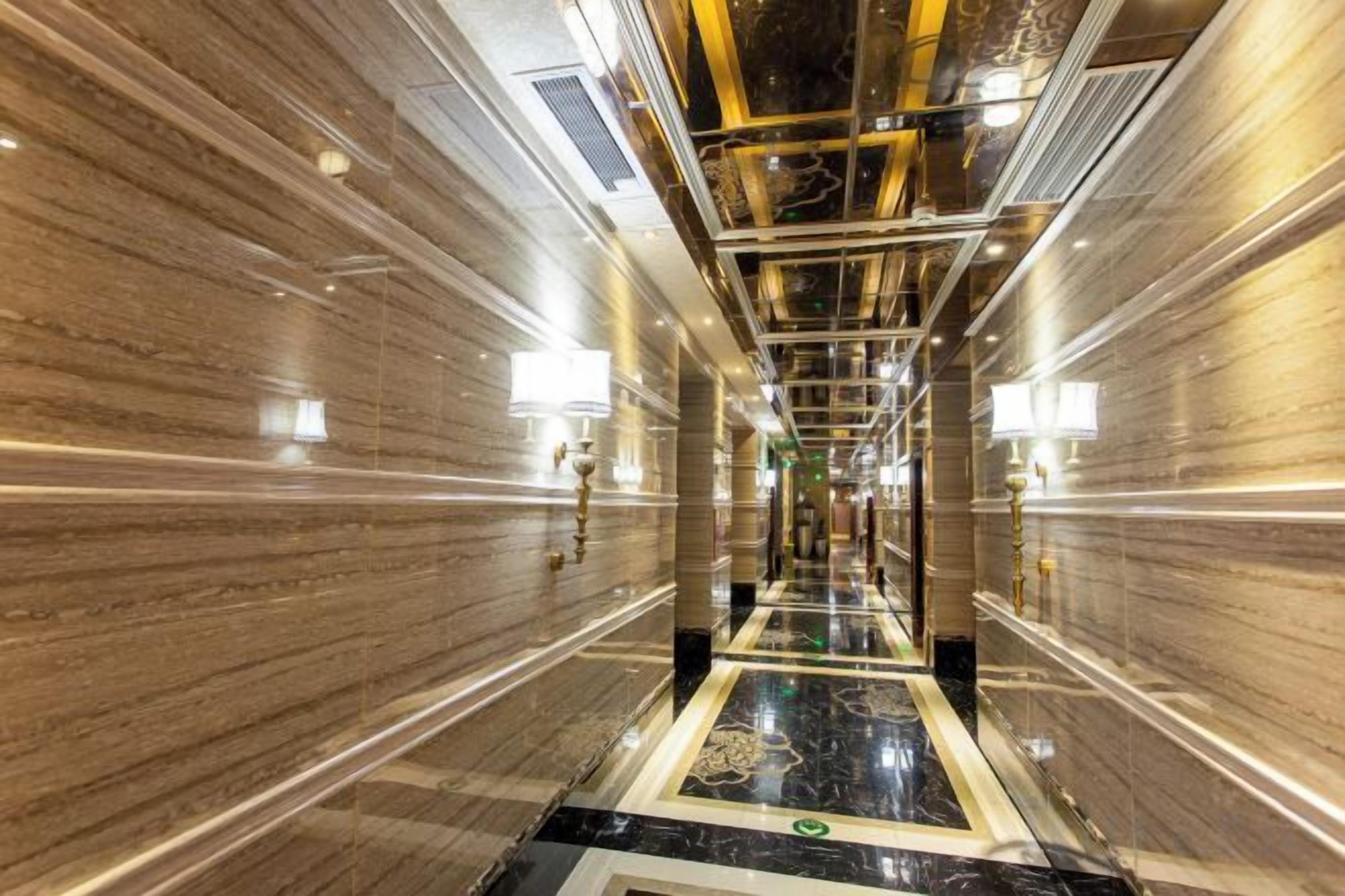 A corridor with marble walls and a reflective floor, leading to a door at the end.