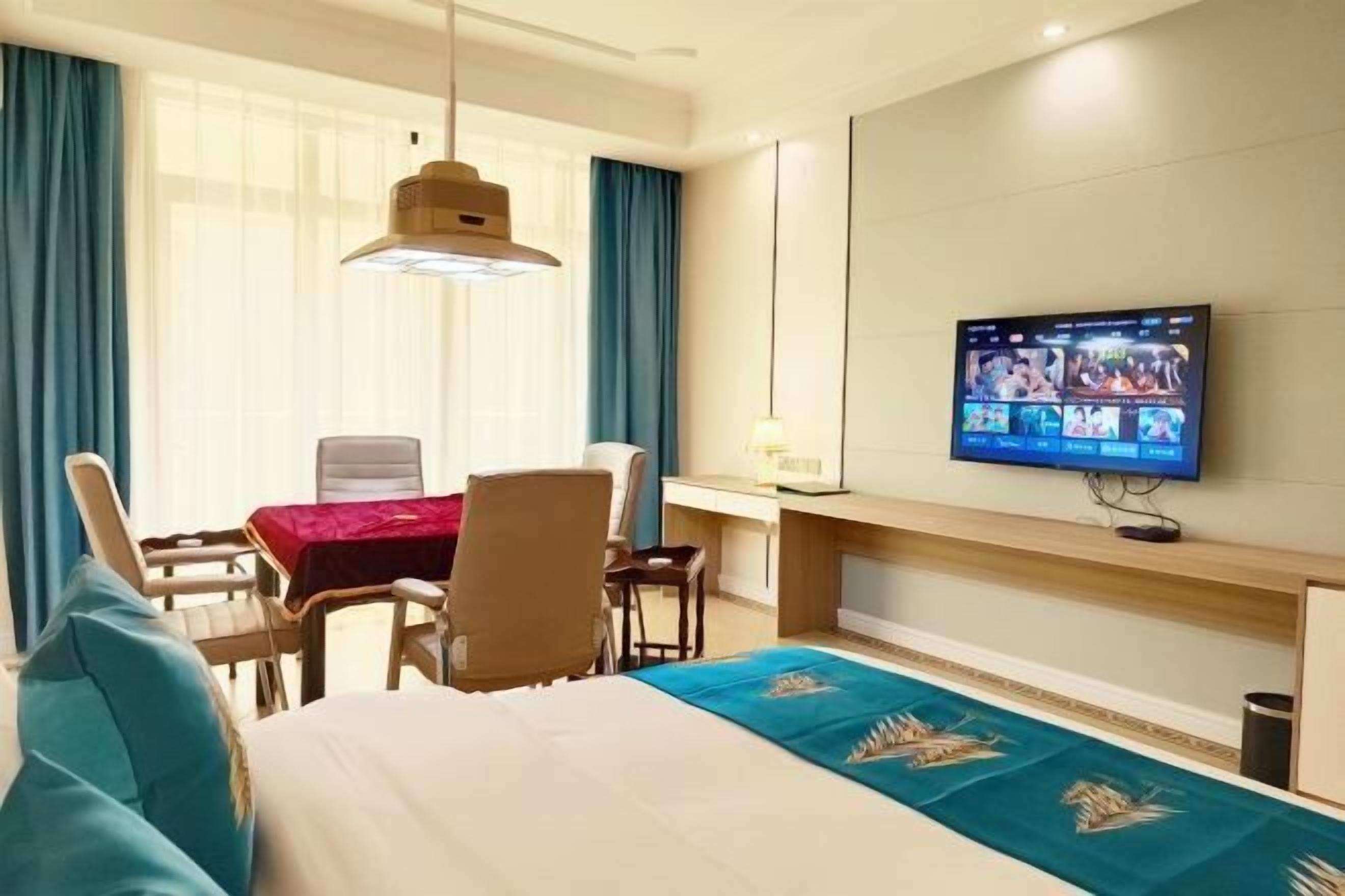 A hotel room with a bed, a desk, a chair, a TV mounted on the wall, and a window with curtains.