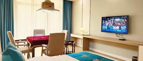 A hotel room with a bed, a desk, a chair, a TV mounted on the wall, and a window with curtains.