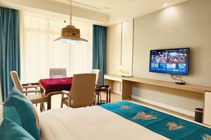 Habitación de hotel con cama, escritorio, silla, televisor montado en la pared y ventana con cortinas.