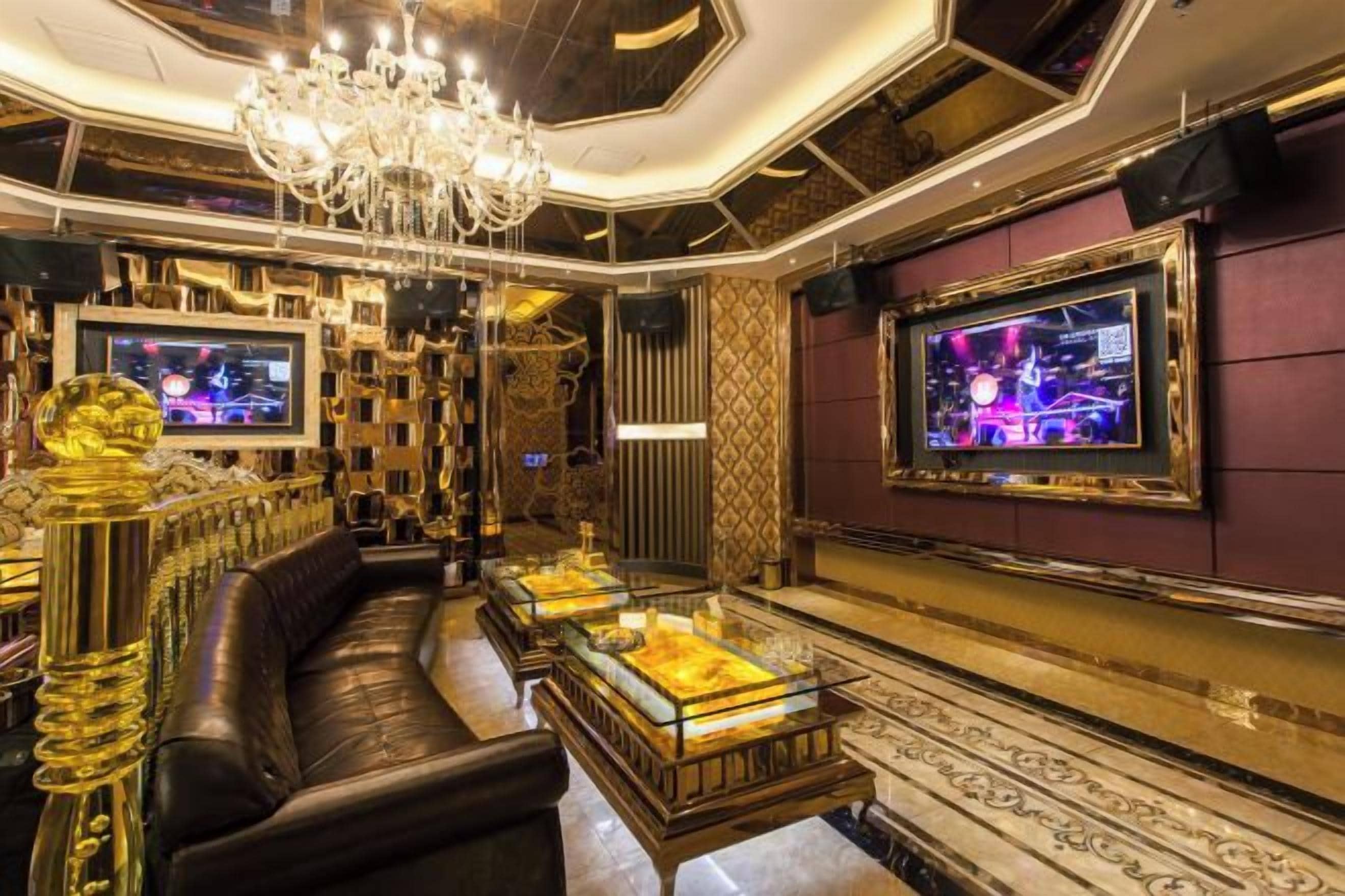 A luxurious interior with a black leather sofa, a chandelier, and a television on the wall.