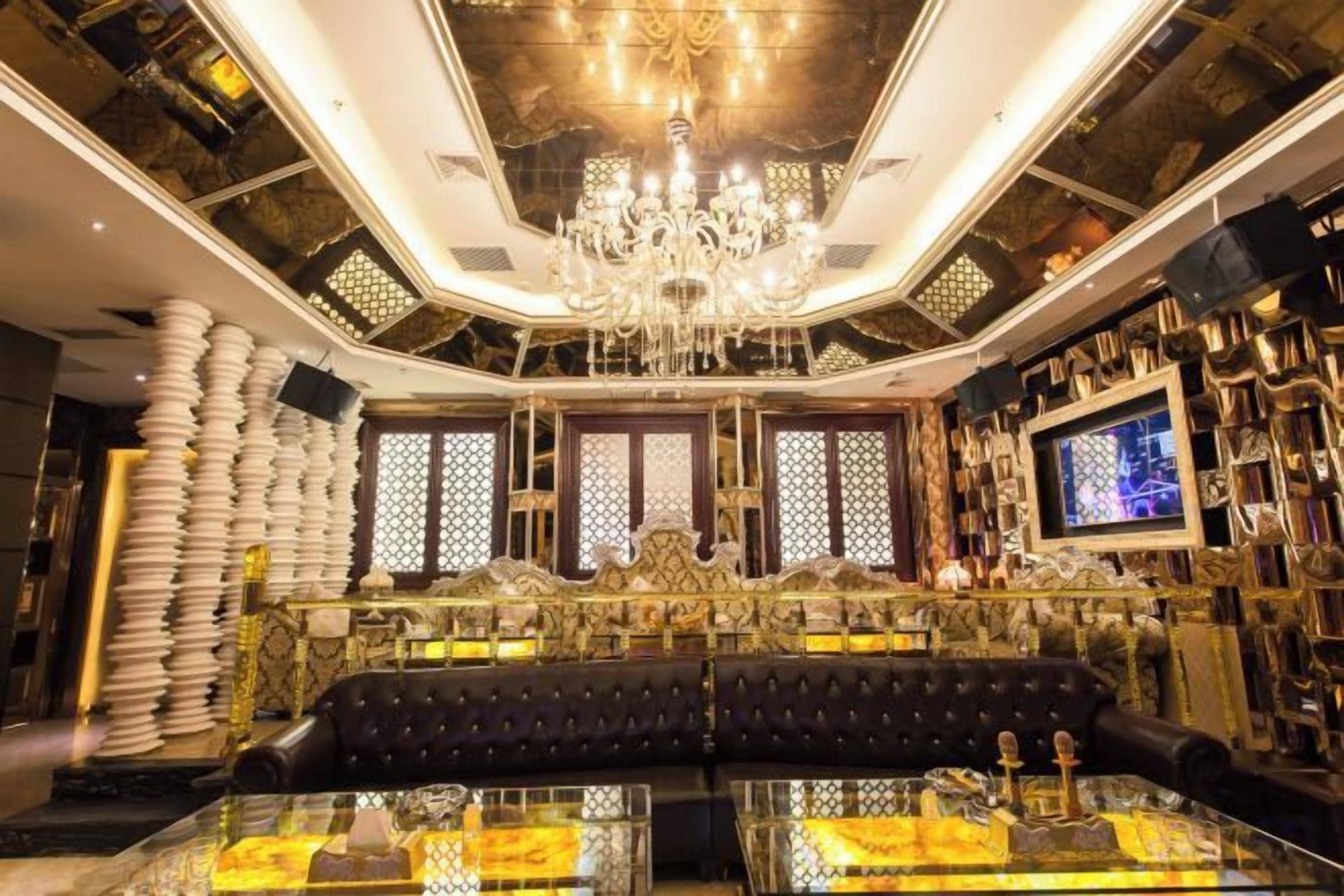 A luxurious interior with a black leather sofa, a chandelier, and a television on the wall.