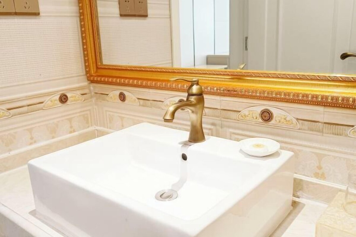 A bathroom with a white sink, gold faucet, and a large mirror with a gold frame.