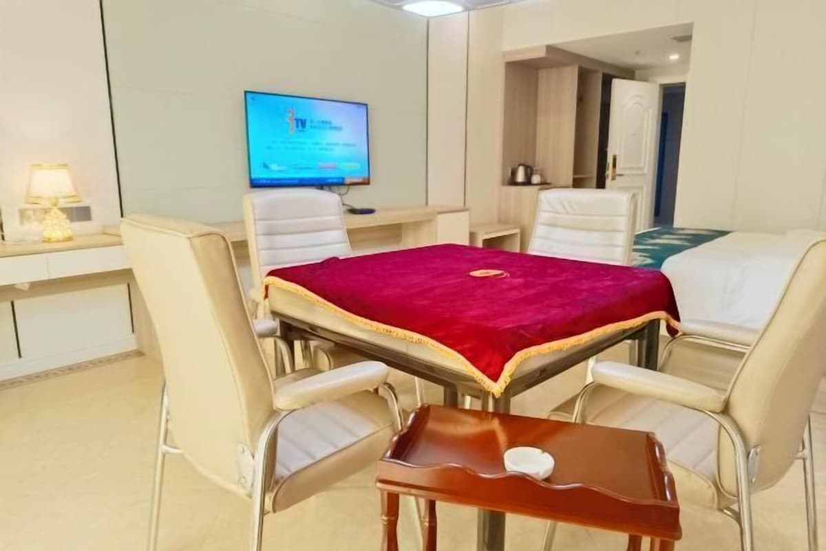 A hotel room with a dining table, four chairs, a TV, and a small wooden table.