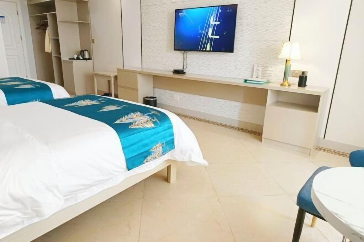 A hotel room with two beds, a TV on the wall, a desk, and a chair.