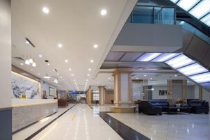 Un vestíbulo de hotel moderno con recepción, zona de estar y techo de cristal.