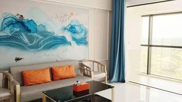 Un salon moderne avec un canapé, des fauteuils, une table basse en verre et une grande fenêtre avec des rideaux.
