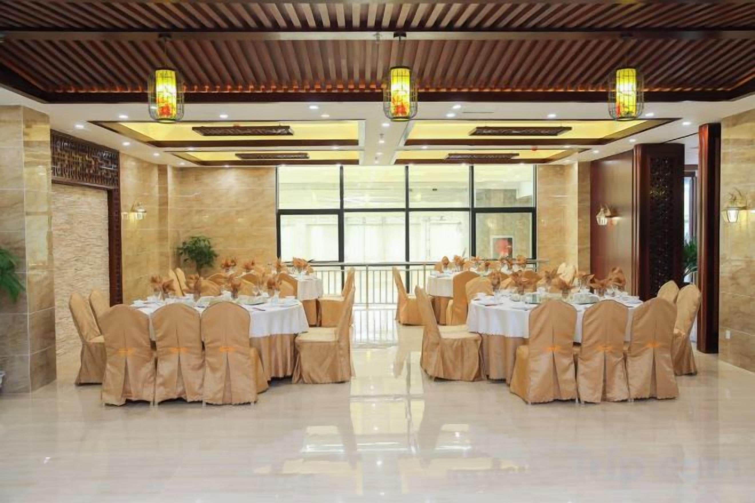 Une salle de banquet avec des tables rondes et des chaises, un plancher ciré et un plafond en bois orné de luminaires suspendus.