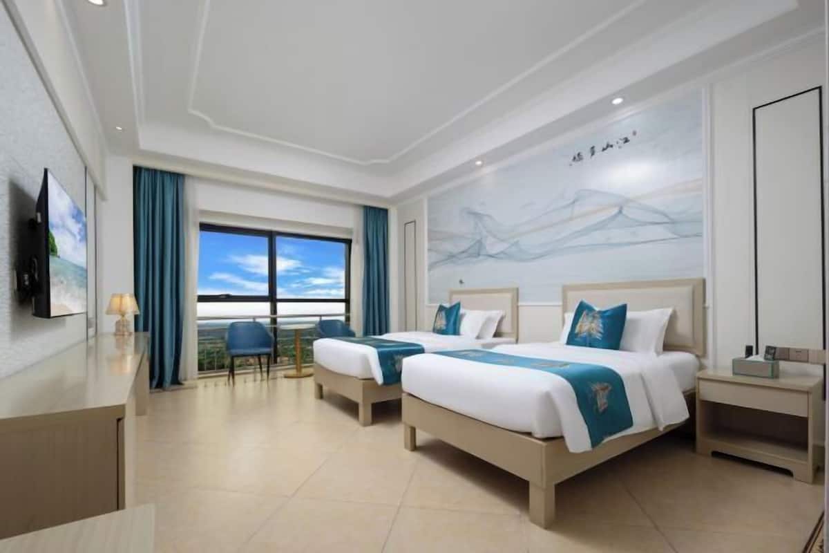 Une chambre d’hôtel avec deux lits, un bureau, une chaise, une grande fenêtre donnant sur un beau paysage et un tableau au mur.