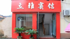Un edificio rojo con caracteres chinos, una escalera y dos macetas con plantas en la entrada.