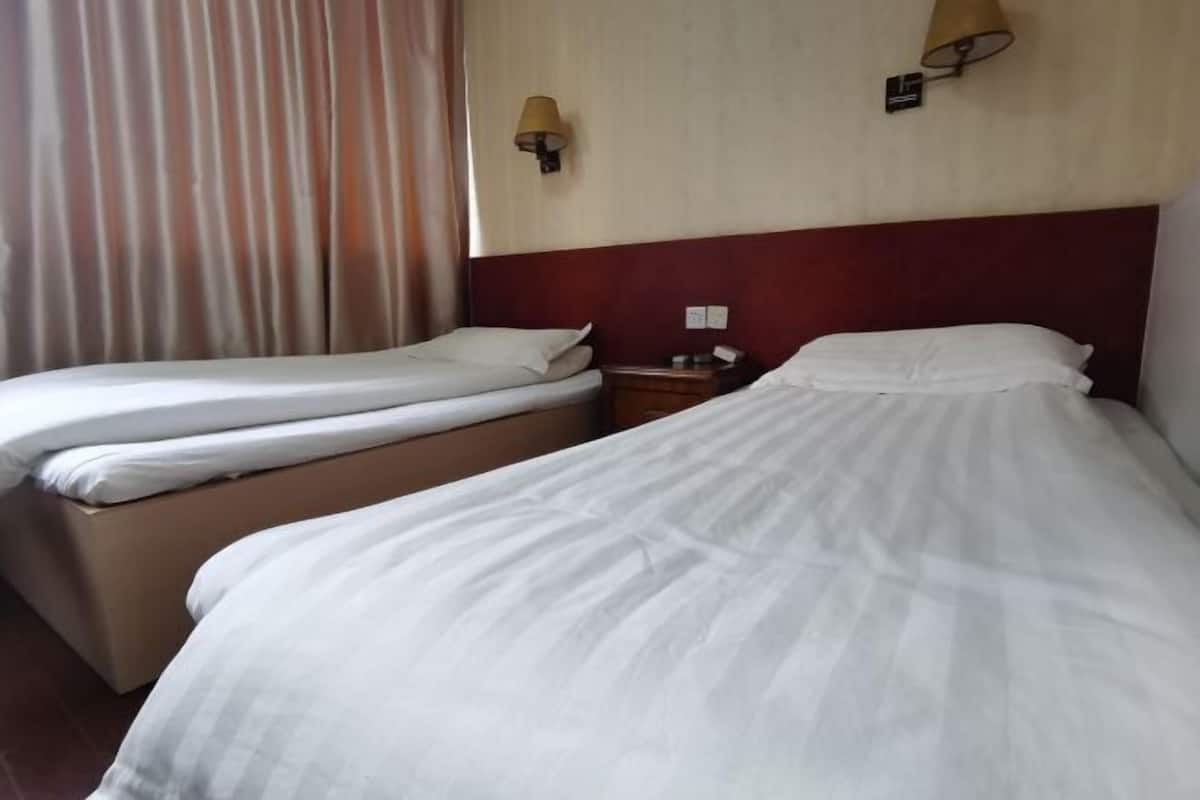 A hotel room with two single beds, a nightstand, and a lamp.