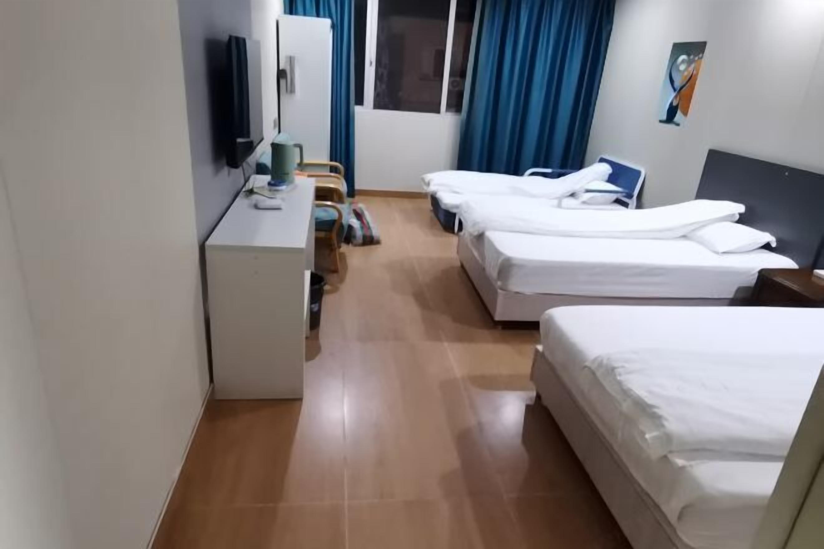 Quarto de hotel com duas camas, uma escrivaninha, uma cadeira, uma televisão e uma janela com cortinas.