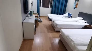 Quarto de hotel com duas camas, uma escrivaninha, uma cadeira, uma televisão e uma janela com cortinas.