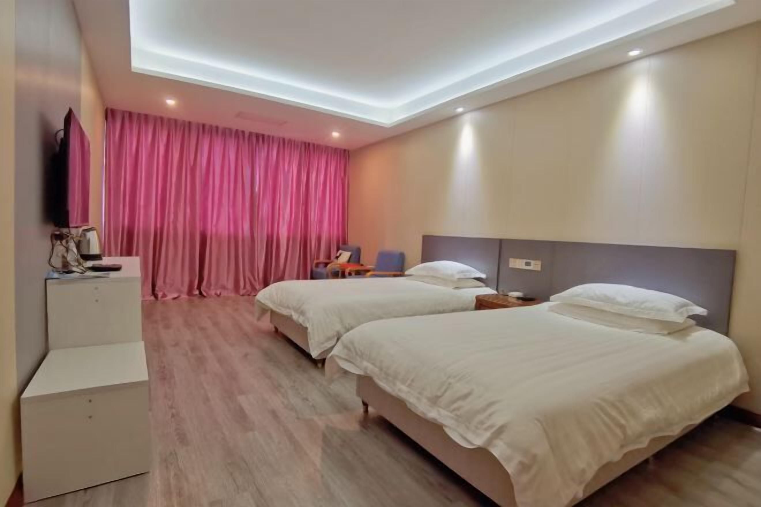 Quarto de hotel com duas camas, televisão de tela plana, escrivaninha e uma janela grande com cortinas cor-de-rosa.