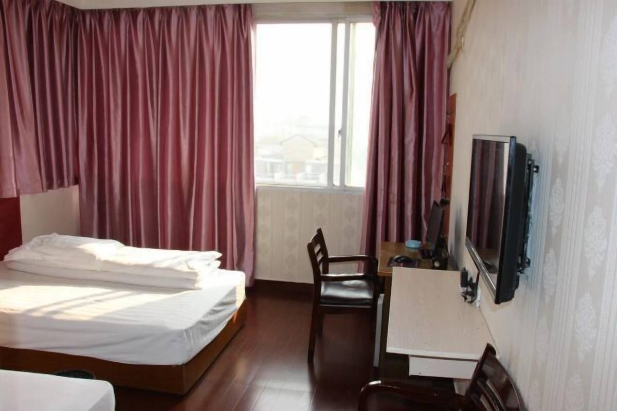 A hotel room with a bed, a desk with a chair, a television, and a window with curtains.
