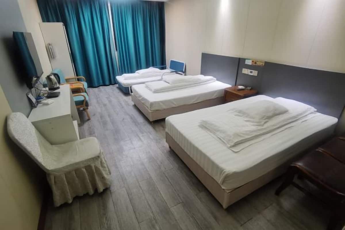 A hotel room with two beds, a desk with a chair, a wardrobe, and a television.