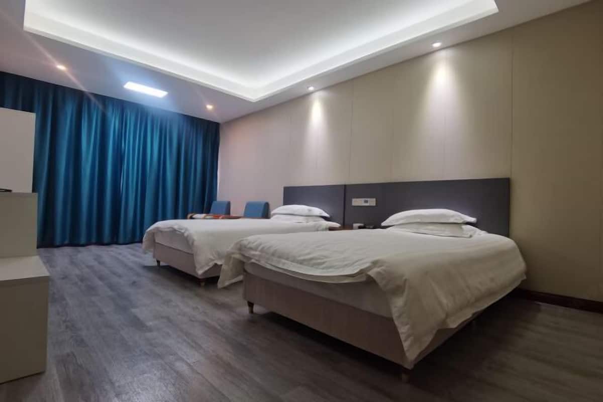 A hotel room with two beds, a desk, and a large window with curtains.