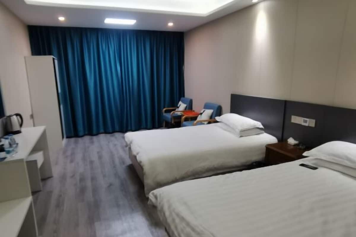 A hotel room with two beds, a desk, a chair, and a curtain.