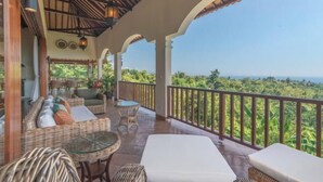 A covered outdoor seating area with wicker furniture, a glass table, and a view of lush greenery. - Villa Mata Hari (Bali)
