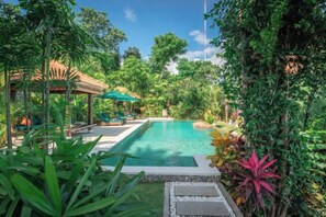 A swimming pool surrounded by lush greenery, with a covered seating area and a gazebo. - Villa Mata Hari (Bali)
