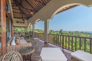 A covered outdoor seating area with wicker furniture, a glass table, and a view of the landscape. - Villa Mata Hari (Bali)