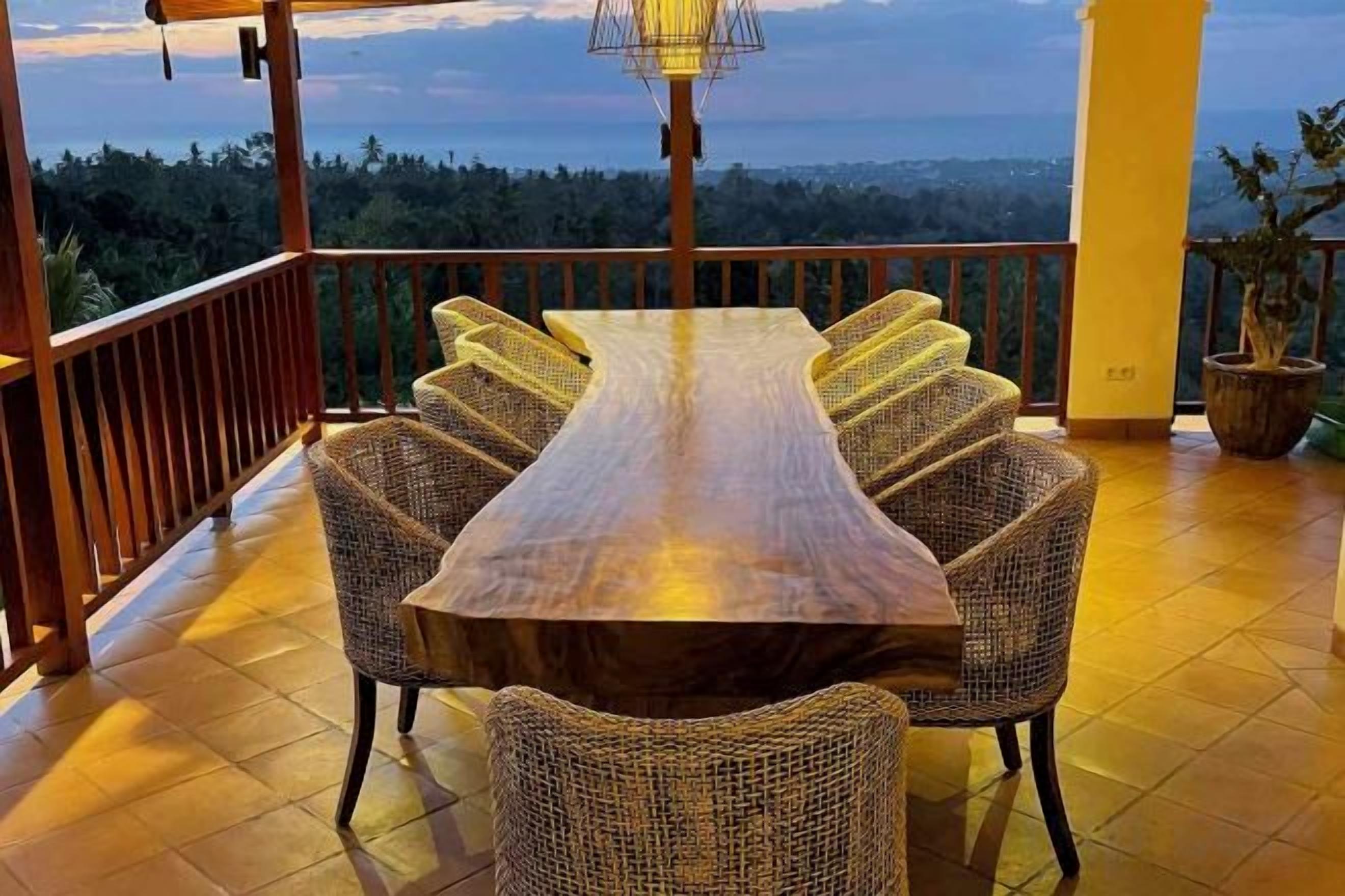 Une table à manger en bois, entourée de chaises en osier, sur un balcon offrant une vue panoramique.