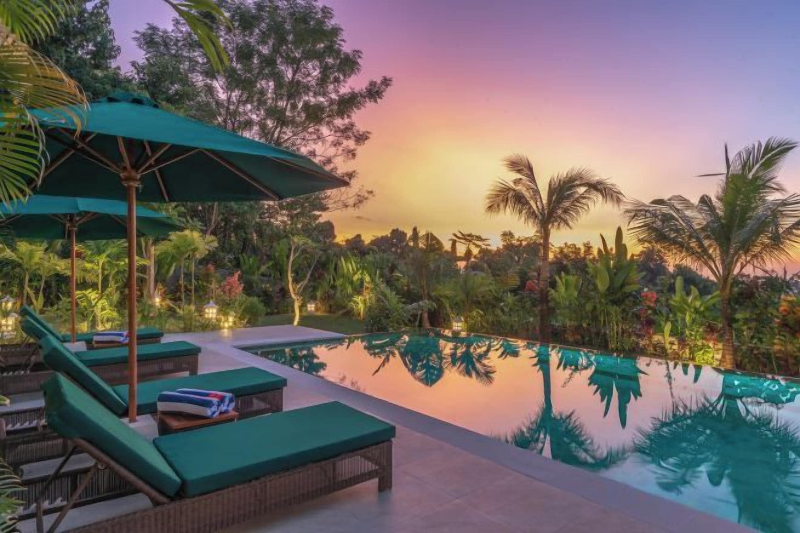 A serene pool area with lounge chairs and umbrellas, surrounded by lush greenery.