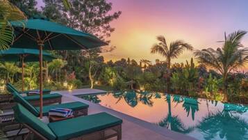A serene pool area with lounge chairs and umbrellas, surrounded by lush greenery.