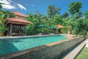A swimming pool with a stone wall, surrounded by lush greenery and a gazebo. - Villa Mata Hari (Bali)