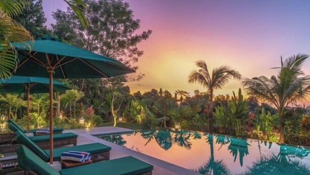 A serene poolside area with lounge chairs and umbrellas, surrounded by lush tropical vegetation. - Villa Mata Hari (Bali)