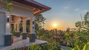 A house with a covered porch, stone pillars, and a garden with various plants and flowers. - Villa Mata Hari (Bali)